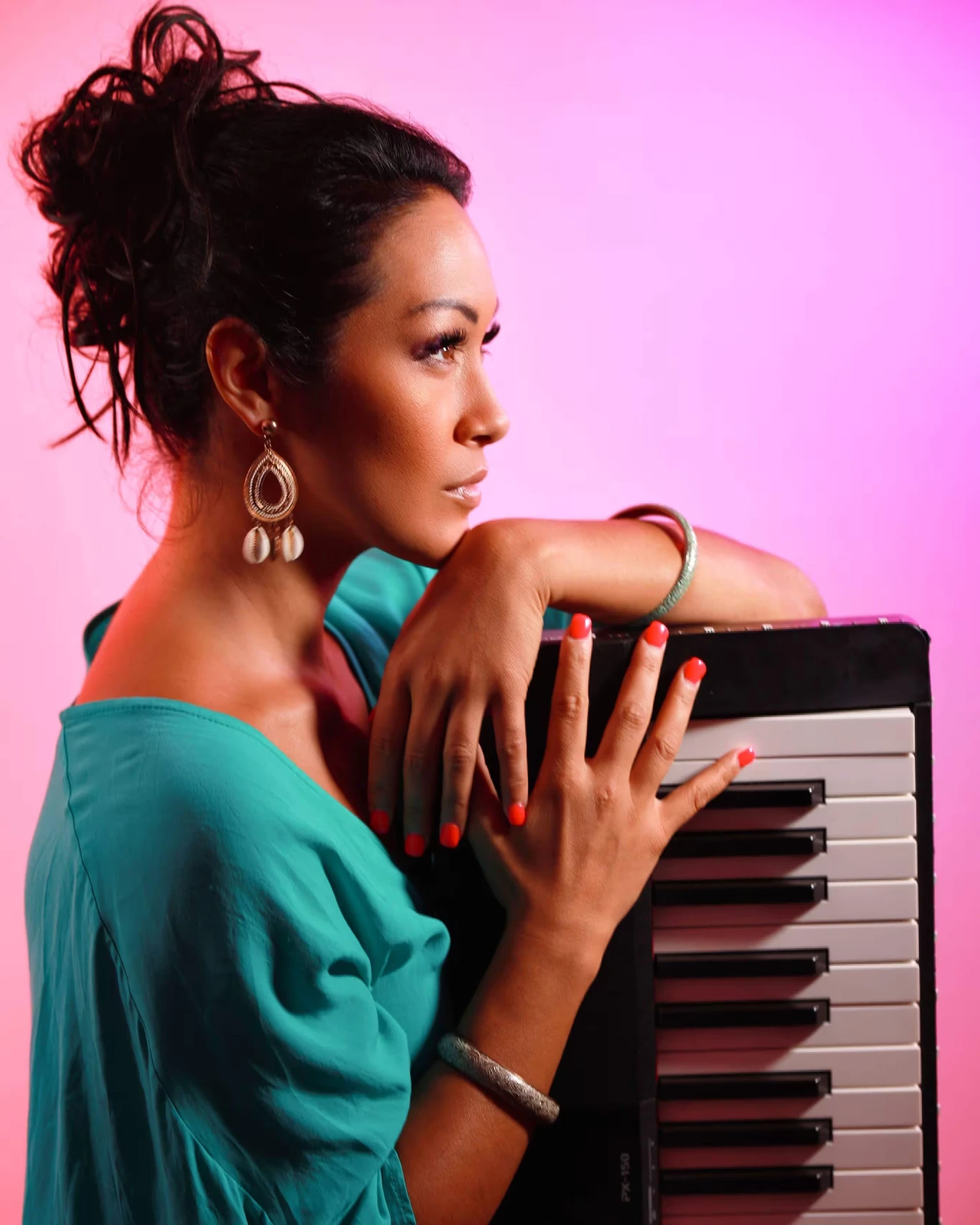 Melina Soochan in teal with long earrings leaning across a keyboard