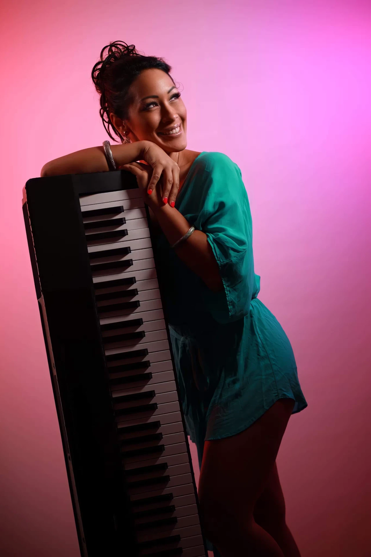 Melina Soochan smiling in a teal dress beside a keyboard